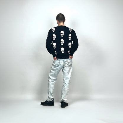Person wearing a black sweater with skull patterns and silver pants on a white background