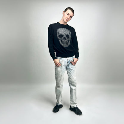 Person wearing a black sweater with a skull design and acid wash denim pants on a white background