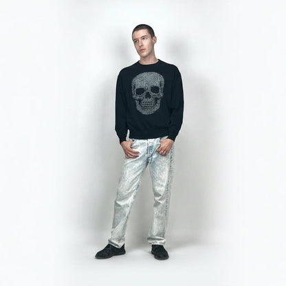 Man wearing a black sweater with a skull design and light blue jeans on a white background