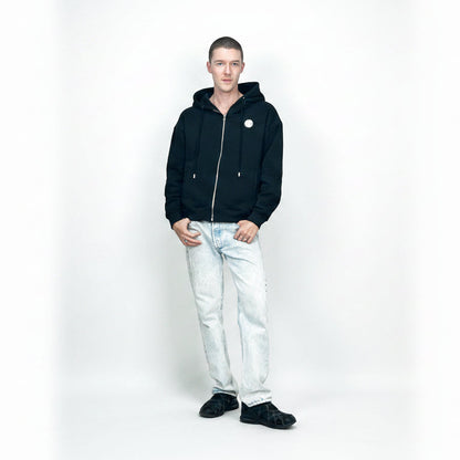 Person wearing a black hoodie and light blue jeans on a white background